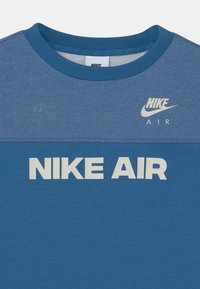 Blå bomullströja med rund hals. Har "NIKE AIR" i vit fet stil och en mindre logotyp ovanför i vitt, med en texturerad övre del.