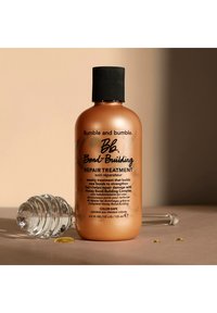 Bumble and Bumble Bond-Building Repair Treatment i en bärnstenfärgad flaska med svart lock. En klar pipett och gula oljedroppar synliga i närheten.