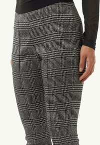 Czarno-białe spodnie stretch w kratkę z teksturowanej tkaniny, z wysokim stanem i dopasowanym krojem. Wyposażone w boczne kieszenie.