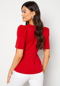 Rode top met korte mouwen en opstaande schouders, peplum taille, gestructureerde stof en een ronde halslijn, gecombineerd met witte broeken.