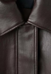 Giubbotto in pelle marrone scuro con un ampio colletto, texture liscia e cuciture dettagliate lungo la patta e le spalle.