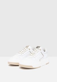 White textured sneakers with a chunky sole, gold accents, and perforated detailing on the toe box. Features golden laces and logo tag.