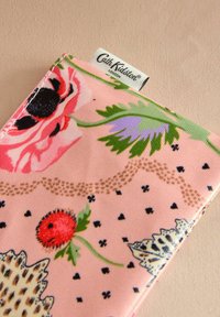 Portofel din material textil cu imprimeu floral, având un fundal roz, flori negre și roșii, frunze verzi și o etichetă cu logo alb. Suprafață texturată cu modele.