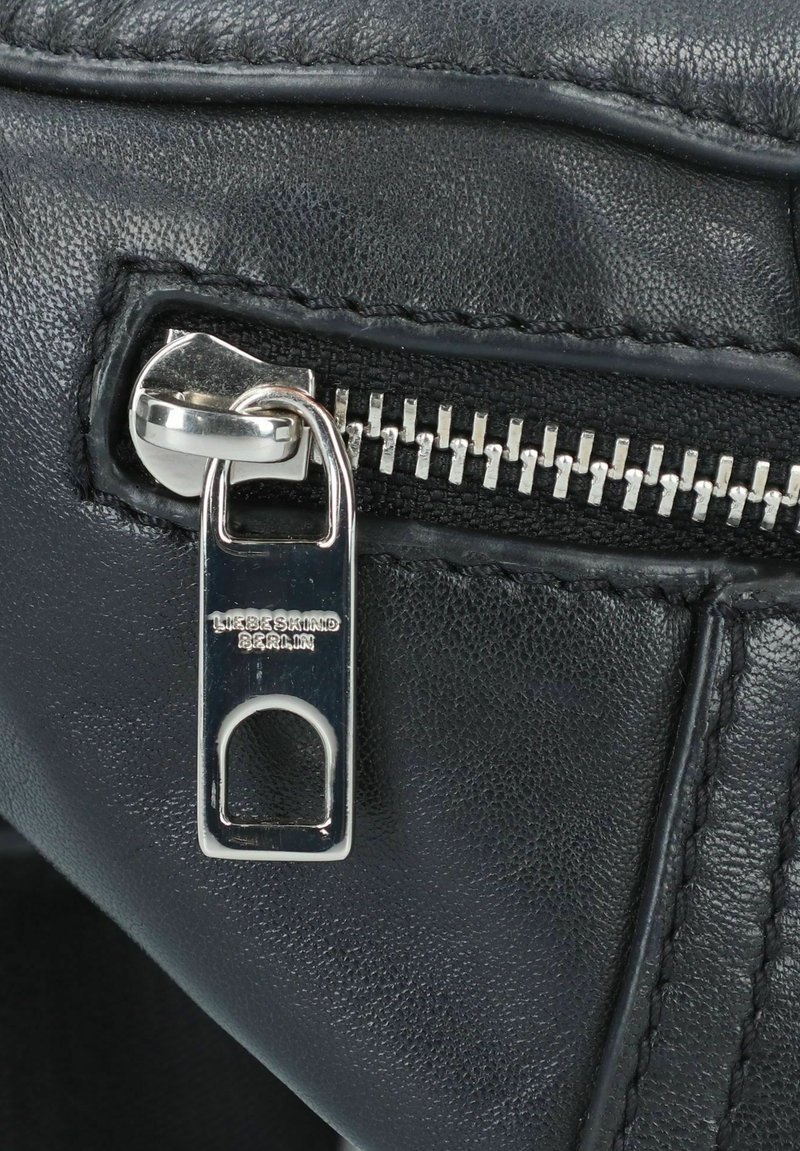 Schwarzes Leder mit Reißverschlussdetails und silberner Hardware. Verfügt über eine genähte Kante und ein Logo-Tag, das auf dem Reißverschlusszuggriff eingeprägt ist.