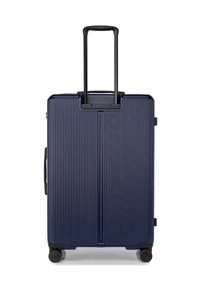 Valigia rigida navy con texture a righe verticali, manico estensibile nero e quattro ruote girevoli per la mobilità.
