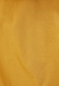 Texturovaná látka v teplé hořčicově žluté barvě, hladký povrch s jemným leskem, zobrazující jednotný vzhled bez vzorů.