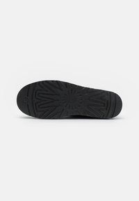 Suela de zapatilla negra con un patrón de agarre texturizado que presenta diseños angulares y un emblema circular central. Construcción de goma duradera.