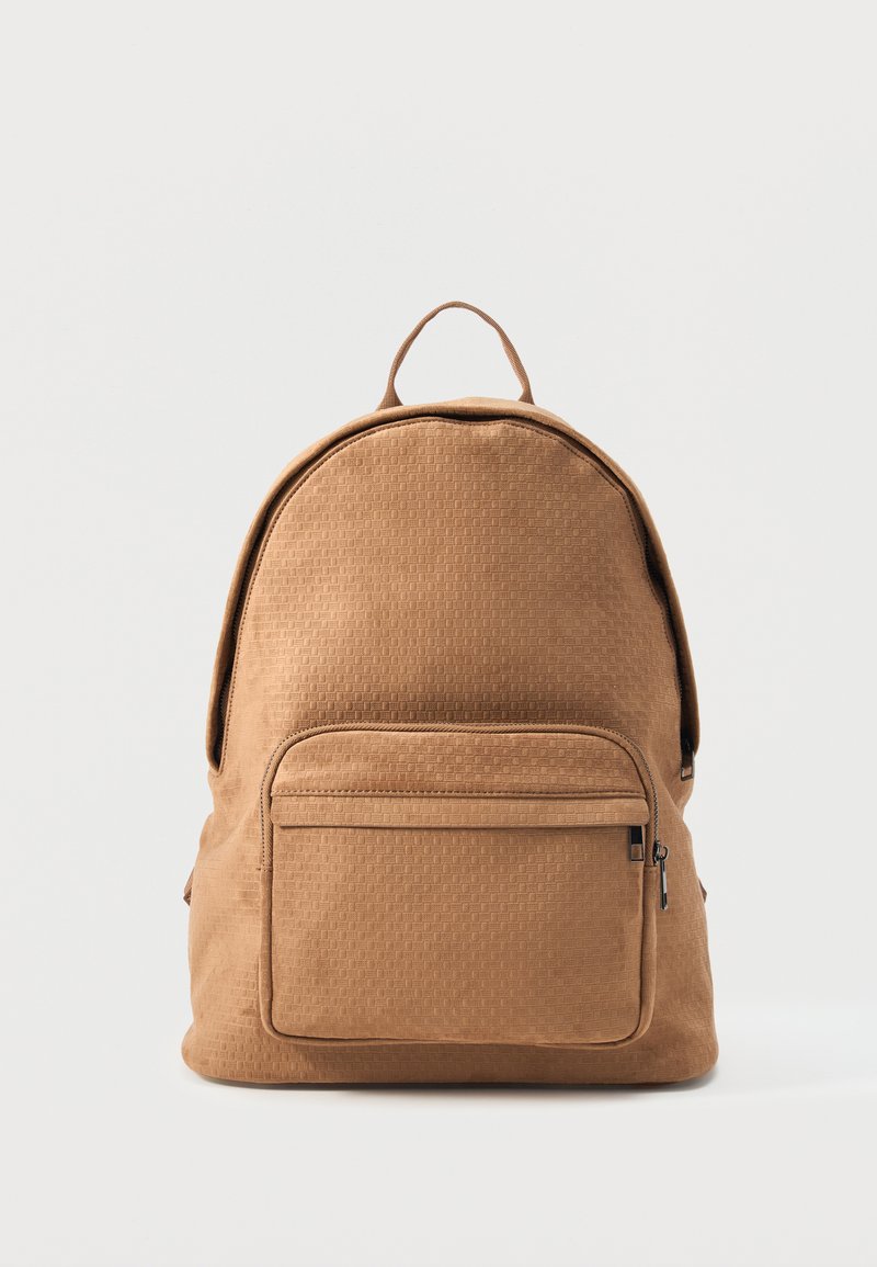 Sac à dos marron texturé avec poche avant zippée et poignée supérieure, debout sur un fond blanc.
