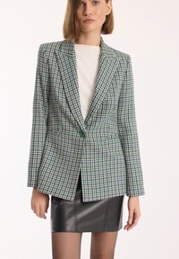 Zielono-fioletowy żakiet w wzór houndstooth o dopasowanym kroju, z pojedynczym zapięciem na guzik i klapami, w komplecie z czarną spódnicą.