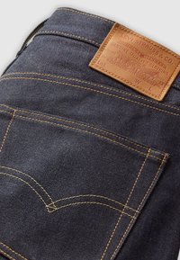 Jean en denim bleu foncé plié pour montrer la poche arrière et l'étiquette en cuir marron Levi Strauss avec le logo de la marque et le texte.