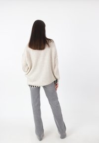 Suéter beige de gran tamaño con un tejido texturizado y un dobladillo a rayas, combinado con pantalones gris de campana. Diseño minimalista sobre un fondo liso.
