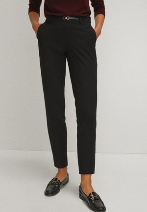 Pantalons noirs ajustés avec une coupe slim, dotés de passants de ceinture, d'une ceinture à boucle dorée et de poches latérales, associés à des mocassins noirs.