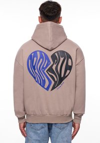 Beige Hoodie mit einem großen Herz-Graphic in blauen und schwarzen Zebramustern auf der Rückseite, mit dem Text "Crew Love" nahe dem unteren Rand.