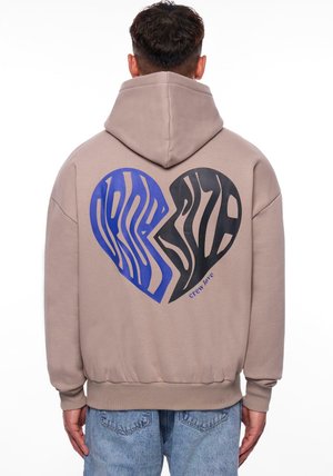 Beige hettegenser med et stort hjertegrafikk i blå og svart zebra-striper på baksiden, med teksten "crew love" nær bunnen.