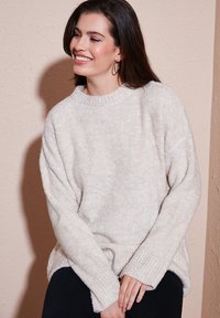 Maglione color crema, morbido e peloso, con un collo a girocollo a coste e polsini. Caratterizzato da maniche ampie e una consistenza morbida.
