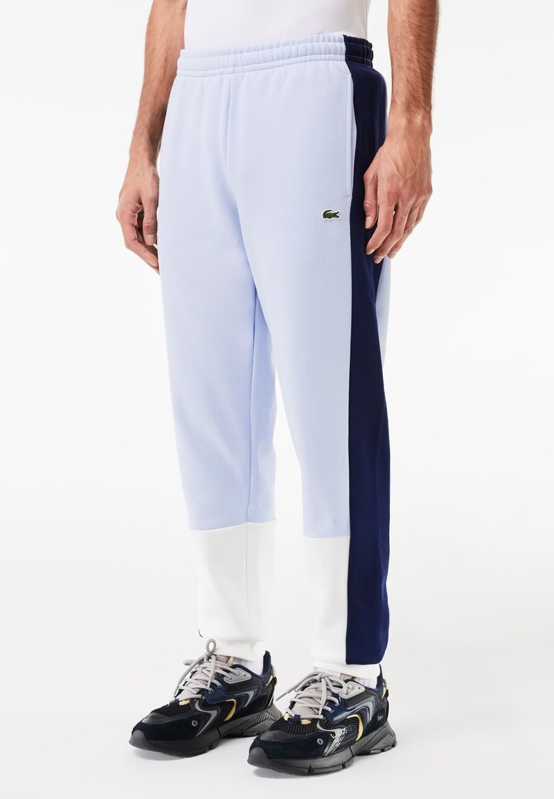 Pantalons de survêtement bleu clair avec des panneaux latéraux bleu marine et blancs, taille élastique et détail de logo vert sur la cuisse ; fabriqués à partir d'un tissu doux.