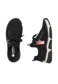 Chaussures de sport noires avec une tige texturée, semelle beige contrastante, fermeture à lacets et couture décorative. Présente un détail de fermeture éclair et une étiquette.