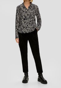 Camicia a maniche lunghe di colore blu navy con un motivo astratto bianco, abbinata a pantaloni in velluto a coste neri e stivaletti neri spessi.