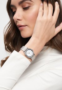 Silberner achteckiger Uhr mit einem weißen Ziffernblatt und silbernem Armband, das ein minimalistisches Design und klare Stundenmarkierungen aufweist. Am Handgelenk getragen.