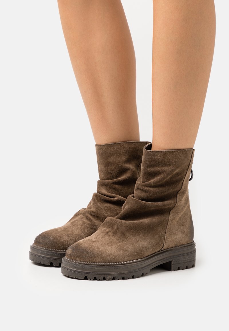 Bottes mi-mollet en daim marron avec semelles crantées épaisses portées sur des jambes nues, présentant un design légèrement décontracté et un bout arrondi.