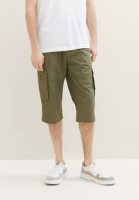 Olivenfarbene Cargo-Shorts mit Seitentaschen, aus leichtem Stoff und knielangem Schnitt, kombiniert mit weißen und beigen Turnschuhen.