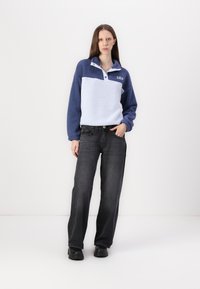 Fleece pulóver v modrej a svetlo modrej farbe s polo golierom a detailom na gombíky; skombinovaný s čiernymi rovnými džínsami a čiernymi topánkami.