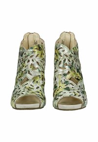 Zapatos de tacón abiertos en cuero crema y verde con diseños florales recortados. Presentan una superficie texturizada y un cierre de cremallera en la parte posterior.