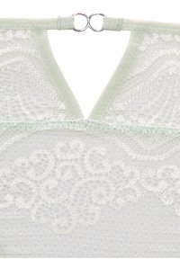 Balta mežģīņu bralette ar V formas dekoltē, aizmugurē ir sudraba apaļā sprādze un gaiši zaļš apmale ap kaklu.