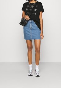 Musta t-paita, jossa graafinen kuvio, yhdistetty vaaleansiniseen farkkuhameeseen. Valkoiset lenkkarit, joissa kukkakoristeet, ja nilkkasukat täydentävät asun.