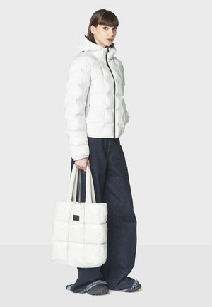 Doudoune blanche brillante avec un col montant et fermeture éclair, assortie à un sac fourre-tout matelassé. Pantalons en denim bleu à jambe large.