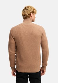 Beige polotröja i ribbat tyg med långa ärmar och en figurnära design. Baksidan visar en sömlös och ren finish.