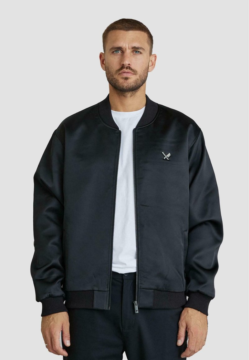 Giacca bomber nera realizzata in tessuto morbido, con colletto e polsini a coste. Include un piccolo emblema con spade incrociate sul petto.