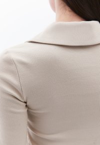 Beige geribde gebreide top met een kraag, close-up van de achterkant, met nadruk op textuur en structuur.