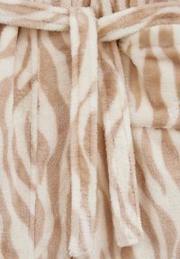 Accappatoio a fantasia zebra beige e crema, realizzato in tessuto morbido e strutturato, con cintura annodata in vita e una sensazione di morbidezza.