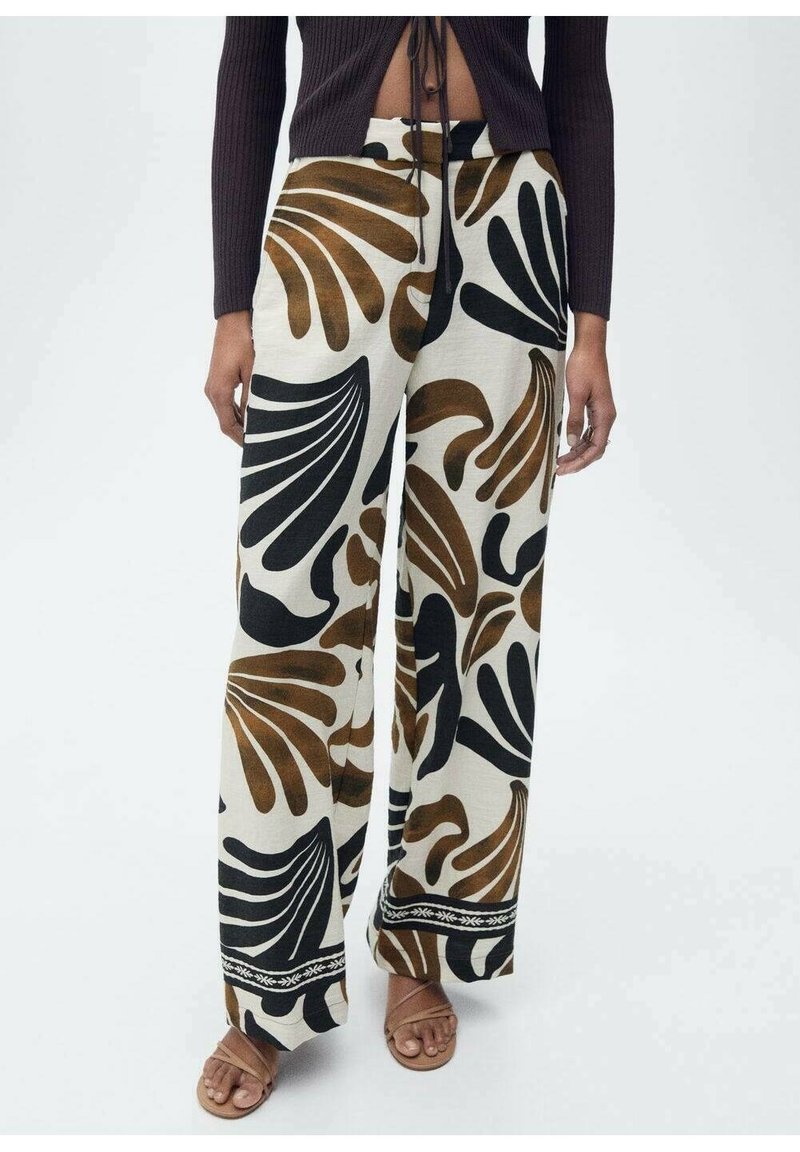 Un pantalon large avec une base crème ornée de grands motifs de feuilles noirs et marron, terminé par une bordure décorative noire au bas.
