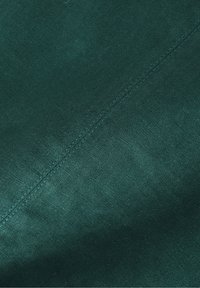 Tessuto verde scuro con una superficie liscia e una lucentezza sottile, caratterizzato da una cucitura visibile lungo un lato.
