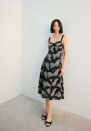 Robe noire avec un motif floral à la main, encolure carrée et larges bretelles. Le tissu est léger, avec une silhouette en ligne A.