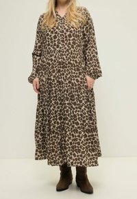 Robe longue à imprimé léopard avec un design à volants, manches longues et un décolleté en V, fabriquée en tissu léger. Portée avec des bottes de cow-boy marron.