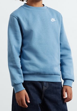 Enfant portant un sweat-shirt Nike bleu clair avec poignets et ourlet côtelés, associé à un jean en denim foncé, sur un fond uni.