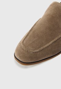 Brown suede slip-on shoe with rounded toe, accent stitching, and a slightly elevated rubber sole. Smooth texture and minimalistic design.