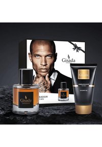 L'emballage de Gisada Ambassador comprend un grand flacon de parfum en verre, un flacon plus petit et un tube de gel douche noir avec des accents dorés.
