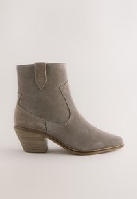 Grå ruskind ankleboot med spids tå, stablet hæl og syningsdetaljer. Har en trækflig bagpå for nem påtagning.