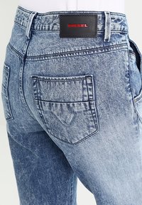 Takapuolet vaaleansinisistä happopesu käsitellyistä Diesel-farkuista, joissa on takataskut ja musta nahkainen brändilaatta punaisella kirjailulla.