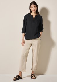 Blusa nera leggera con mezza abbottonatura e maniche a tre quarti, abbinata a pantaloni beige a gamba larga e sandali neri.