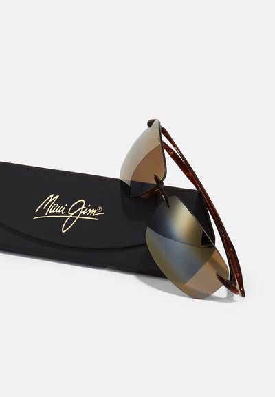 Sunnies med bruna gradientlinser, bruna sköldpaddshorn-armar och ett matt svart fodral med guldtryckt logotext.