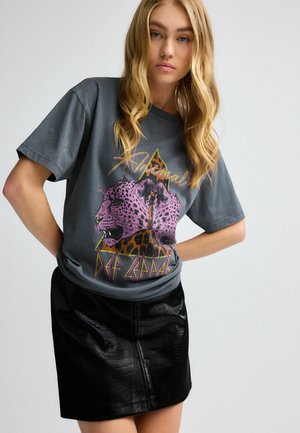 T-shirt graphique gris avec un motif léopard rose et le texte "Def Leppard", associé à une jupe en simili cuir noire avec un motif crocodile.