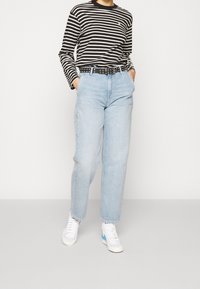 Camisa de manga larga a rayas en blanco y negro, combinada con jeans de tiro alto de color azul claro y un cinturón negro con clavos plateados. Zapatillas blancas visibles.