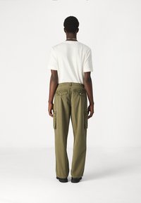 Olijfgroene cargobroek met een relaxte pasvorm, twee zijzakken en twee achterzakken. In combinatie met een eenvoudig wit t-shirt.