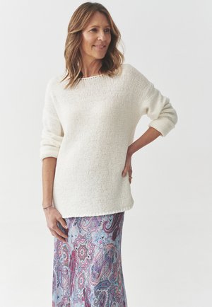 White knitted sweater with long sleeves paired with a long, colorful paisley-patterned skirt featuring blue, pink, and red hues.