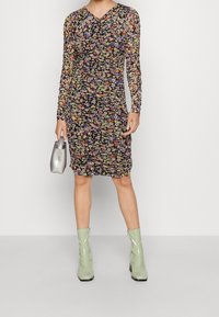 Vestido floral de manga larga con base negra y flores multicolores, diseño fruncido y escote en V. Combinado con botas de tobillo verde menta y un bolso plateado.